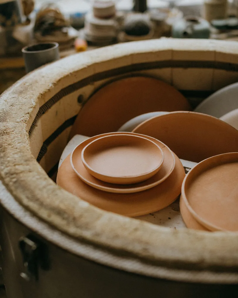 Platos de barro sin esmaltar apilados dentro de un horno cerámico, preparados para la primera cocción